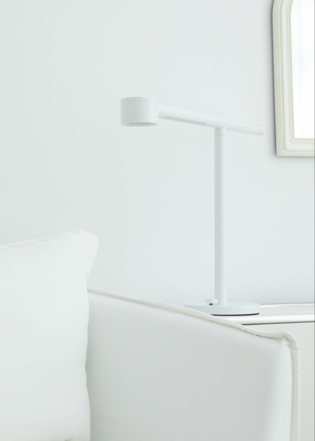 White Forecee Beauty Lamp placed on a side table next to a sofa in a bright, modern room — blending seamlessly into contemporary interiors.