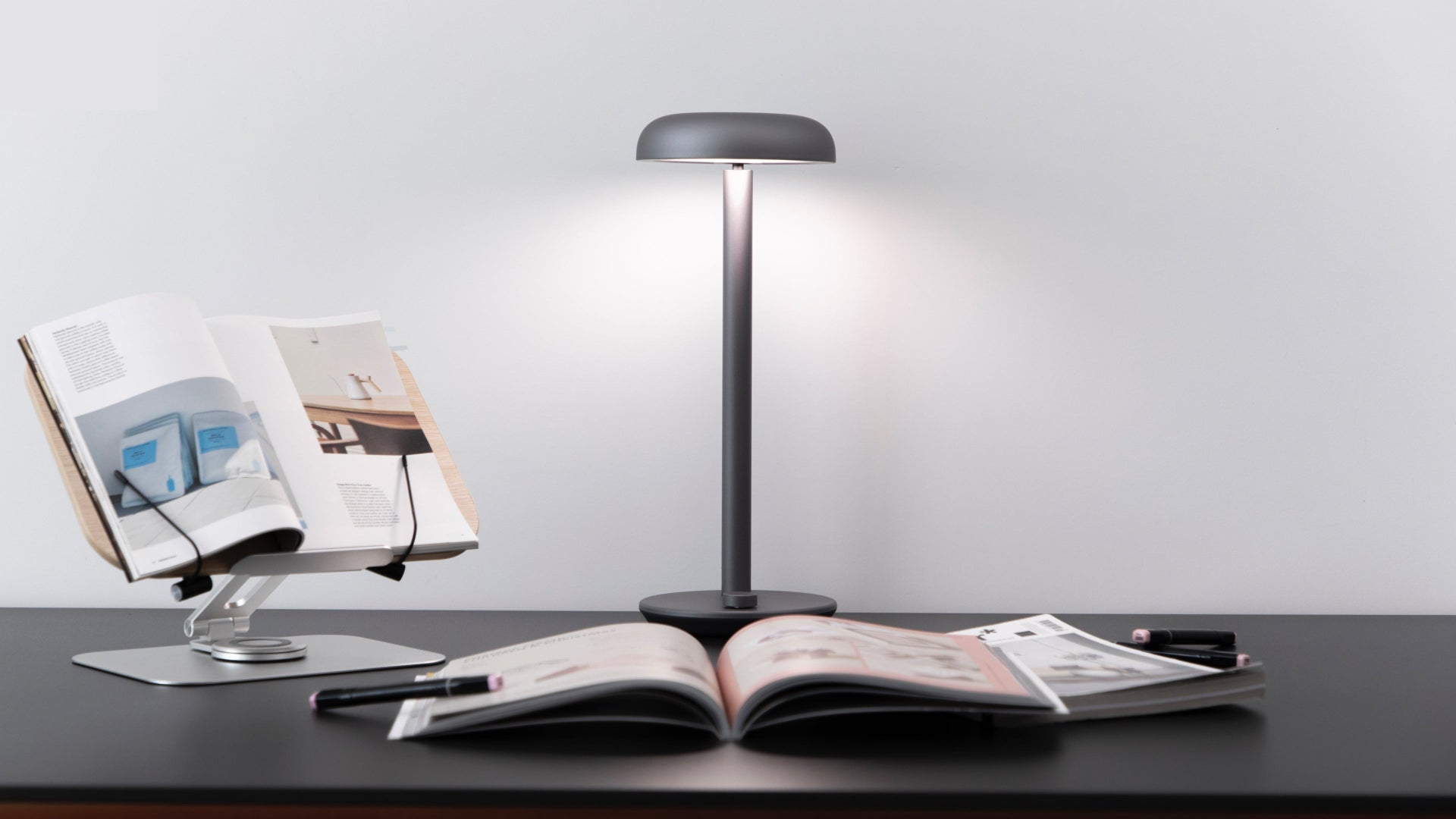 Modern Forecee Desk Lamp lighting an open book on a black desk, showcasing wide, even illumination.