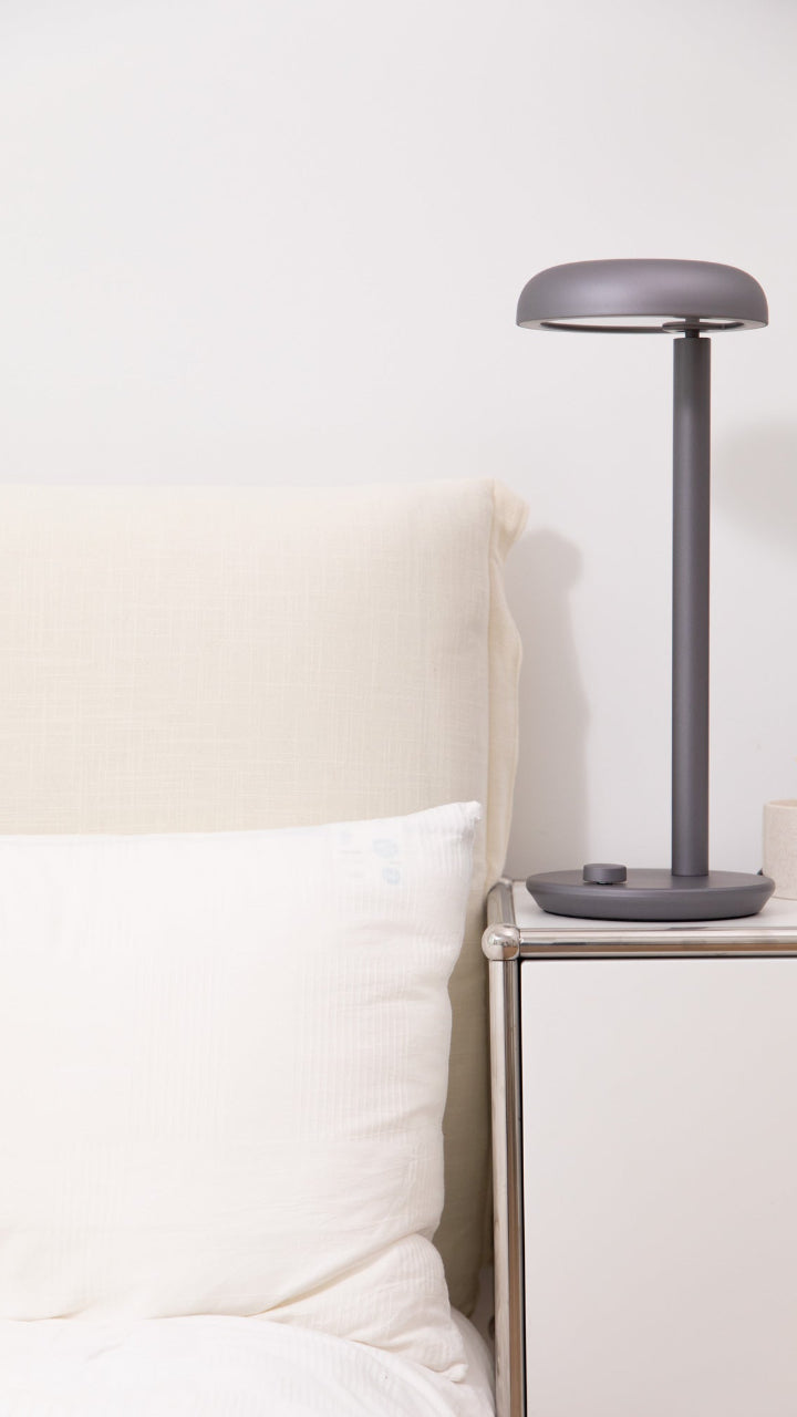 Forecee Desk Lamp on a bedside table, softly illuminating a bedroom with white bedding.