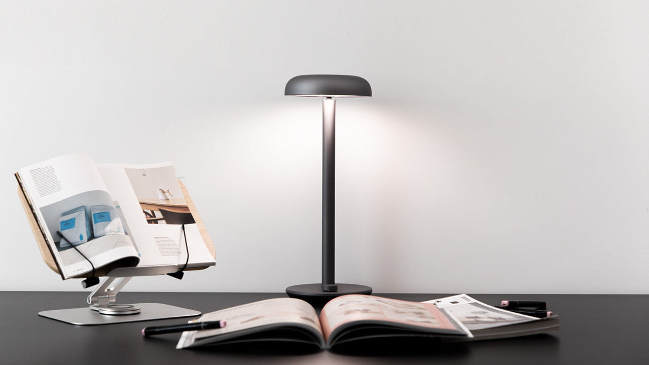 Forecee Desk Lamp providing wide, bright, even light over an open book on a minimalist black desk.